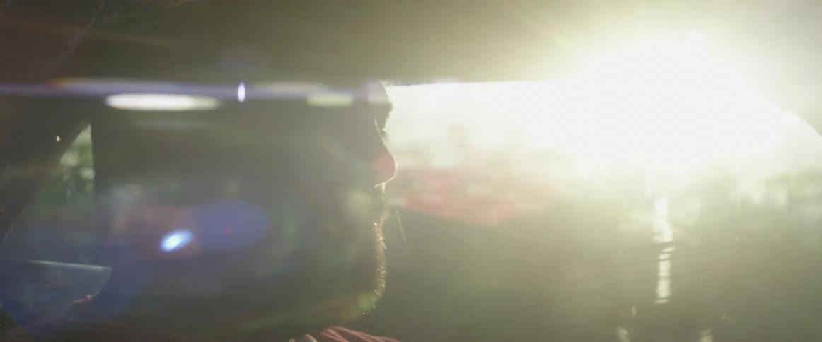 Man is silhouetted against the sun while driving down a country road