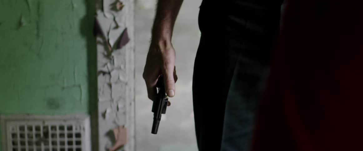 Man wearing glasses and a mustache in an abandoned house takes a gun from his belt