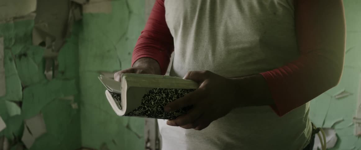 Sad man in an abandoned house takes a letter out of a notebook and gives it to someone out of frame