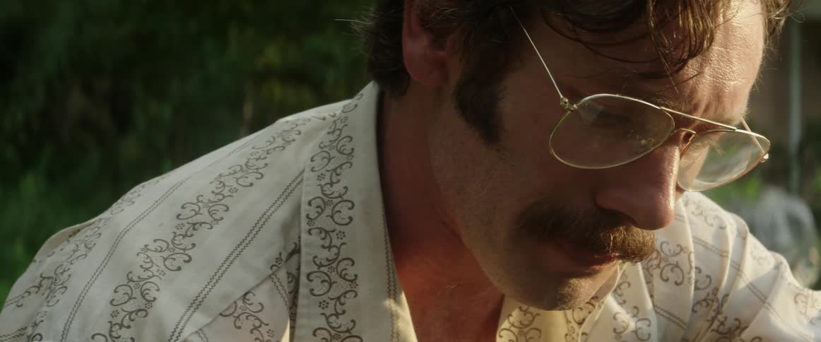 Sad man wearing glasses and a mustache sits outside his home sobbing