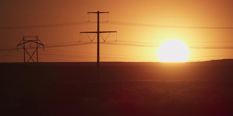 The sun is setting on the horizon past power lines