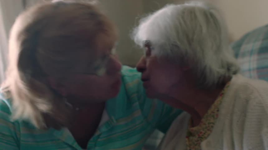 Two women butt heads and kiss in a home