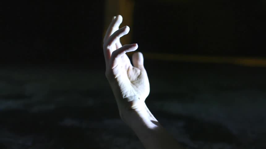 The hand of a person laying on the ground at night being illuminated by a light