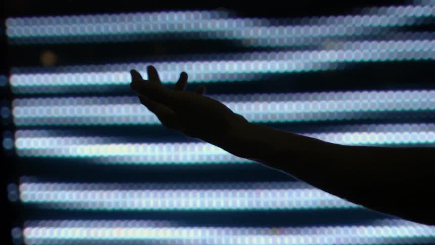 A hand is stretched out in front of a screen with lights