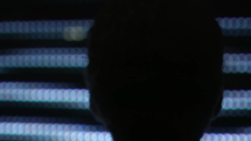 A man is standing in a dark area staring at lights