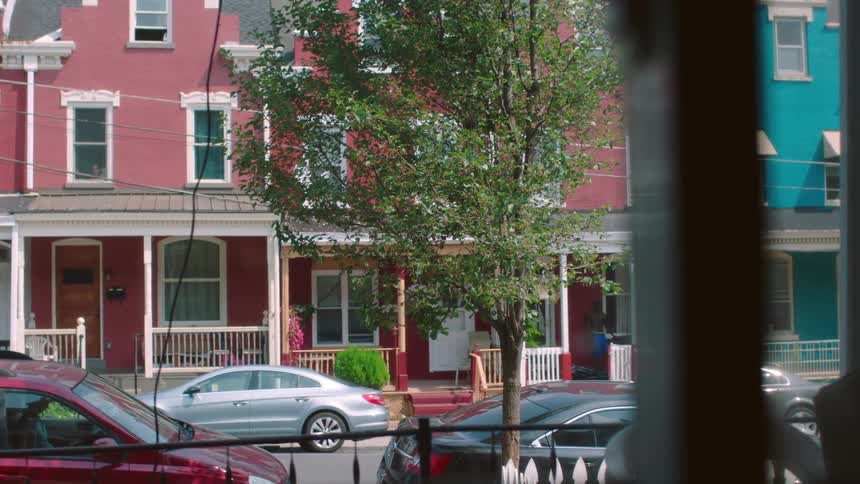 A man stands on the front porch of a house in a neighborhood