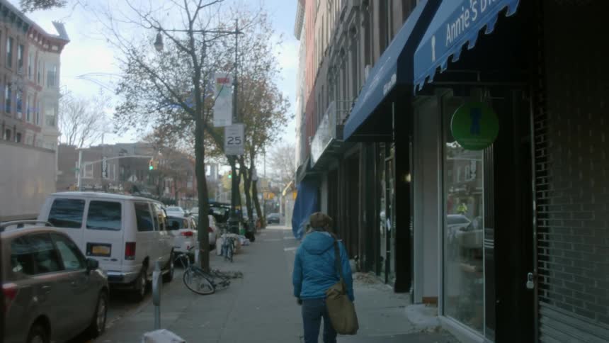 A  woman walking down a sidewalk in a city during the day