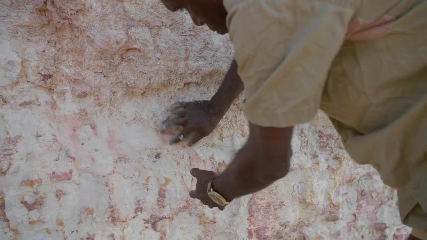 An aboriginal man rubs rock to collect white ochre
