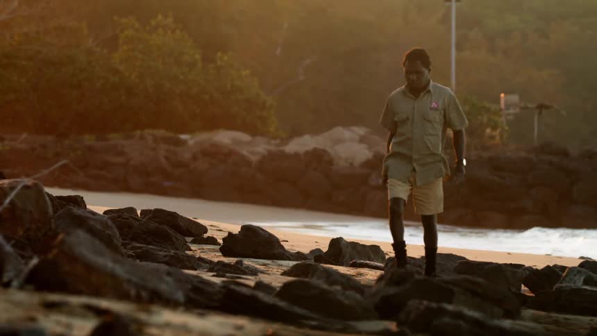 A man walks along a rocky shore as waves splash behind him
