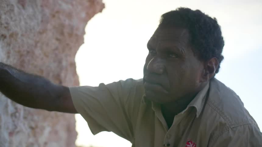 An aboriginal man touches a wall of white ochre