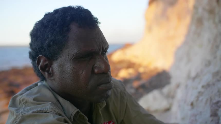 An aboriginal man uses a rock to gather white ochre