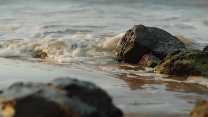 Small ocean waves breaking over the rocks in the sand of a beach at sunset