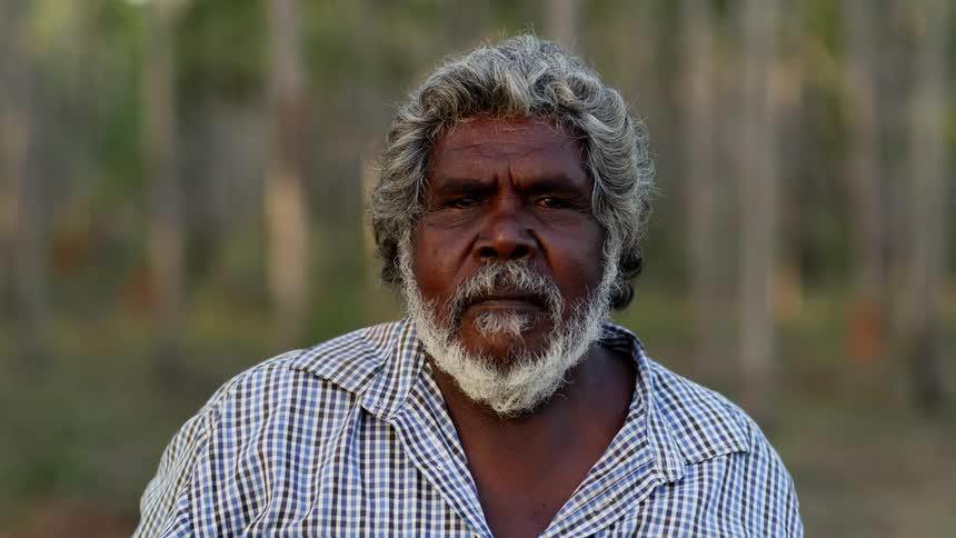 Older aboriginal man with white beard facing camera outdoors