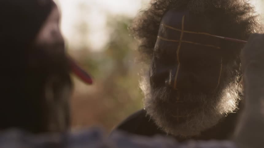 A man draws tribal paint on another mans face