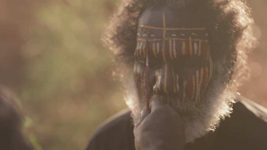 A person paints tribal paint on an elderly man