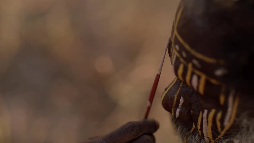 A person paints tribal paint on an elderly mans face