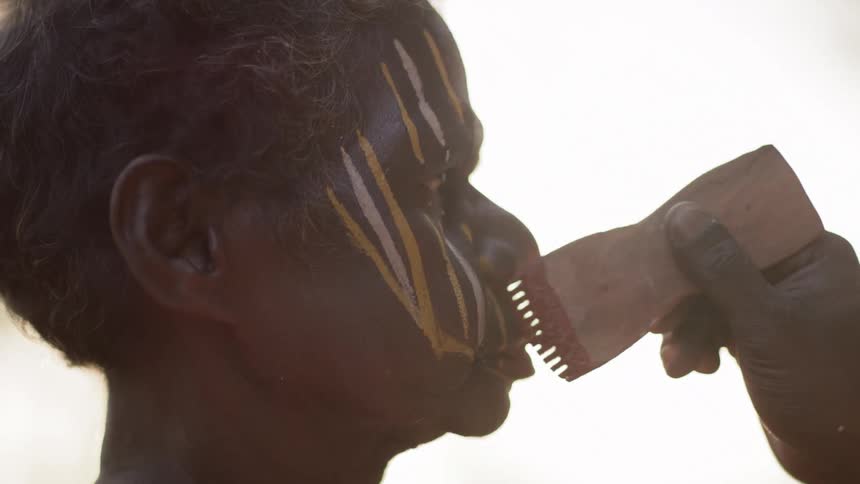 Indigenous person receiving face paint in yellow white and red