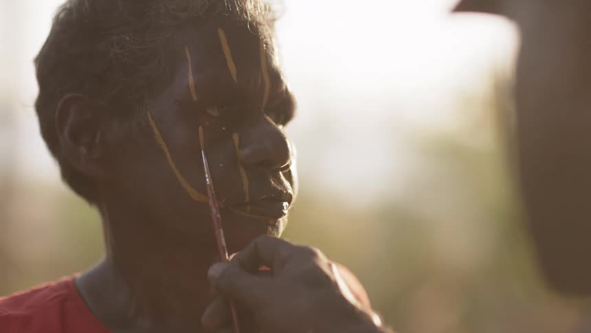 Person applies paint to another persons face with narrow paint brush