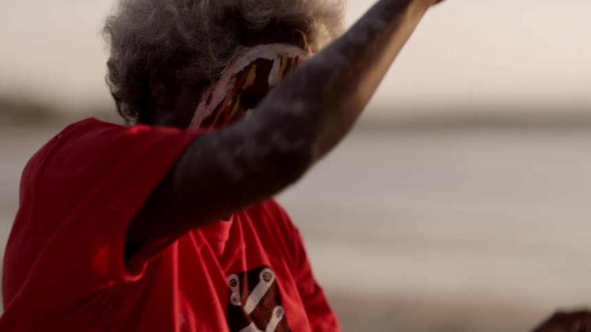 Two women in matching face paint and t shirts dance with their arms raised on the beach as a man crouches behind them