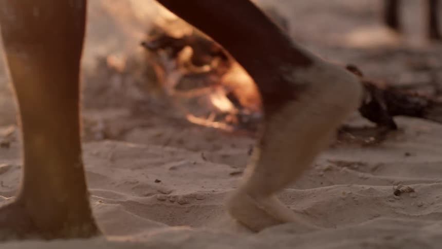 A group of people walking around a fire on the beach