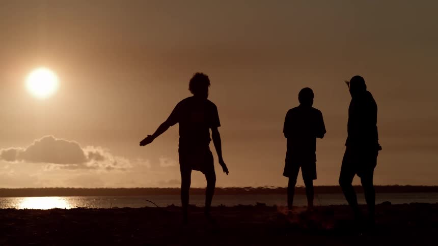 Heat and flames rise up from the ground as men in silhouette dance and walk through the fire