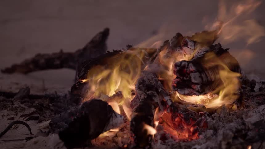 The burning remains of a pile of wood lying in the sand