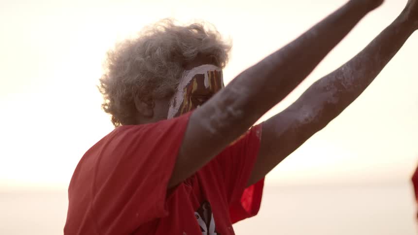 A person with face paint with their hands up with the sky and sunset in the background