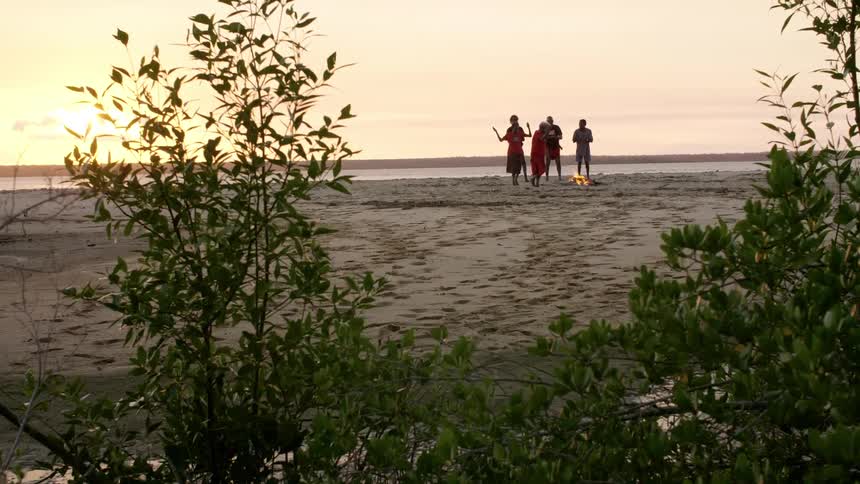 Group of australian indigenous people dancing around a campfire on a beach at sunset