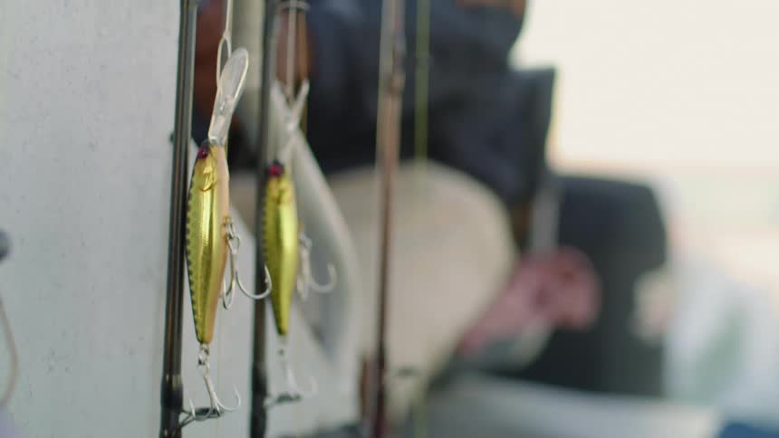 Plastic fish serve as bait on a fishing pole attached to the side of a boat sailing through the ocean