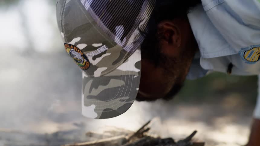 Person leans over small piled branches blowing to start the fire
