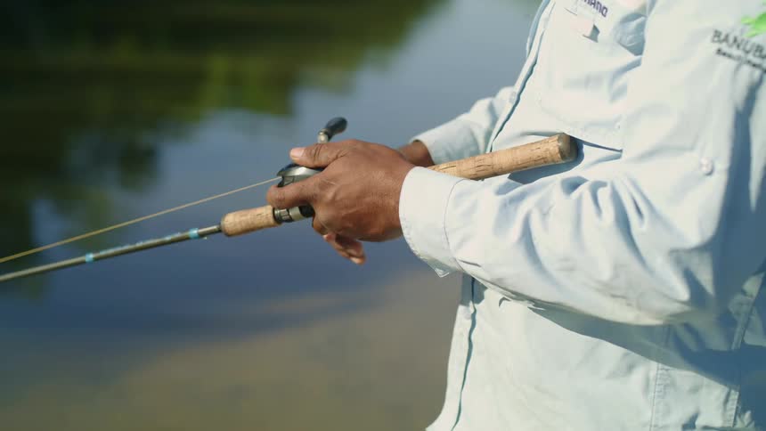 Man with a cap and a blue shirt casts a fishing line in a small boat