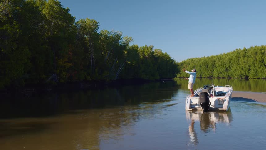 A man climbs up on to his boat and casts his fishing rod in to the water