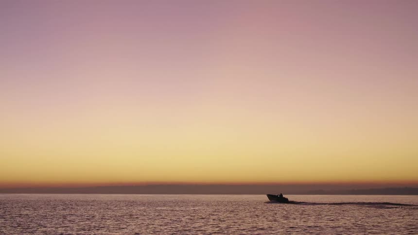 Boat traveling on the sea is silhouetted against the red sky