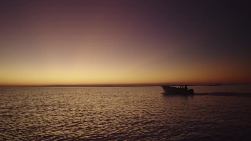 Boat traveling on the sea is silhouetted against the red sky