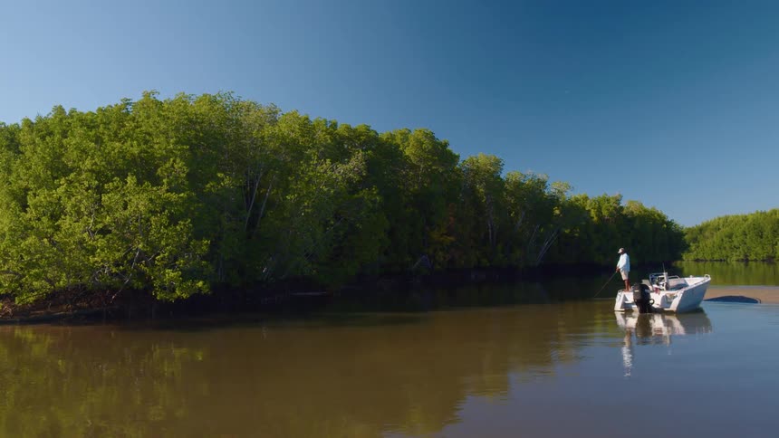 A man is fishing on a peaceful river while standing in a motorboat on a sunny day