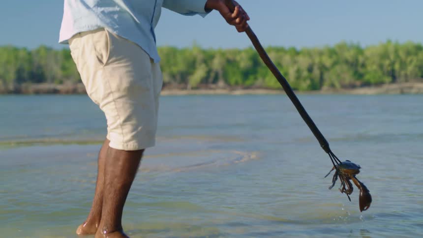 Man catches crab in shallow water with spear