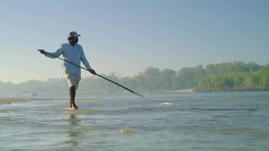 A man carries a spear for fishing as he wades through water