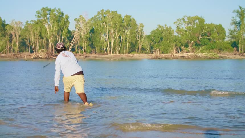 A man walking through the water throws his spear as he spear fishes