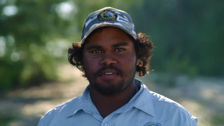 An indigenous man wearing a work uniform looks into the camera while standing outdoors