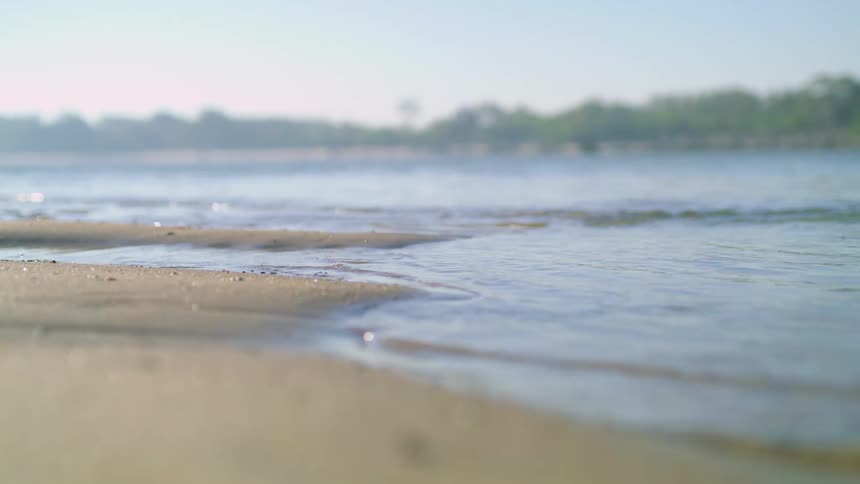 Waves gently roll onto a sandy beach on a sunny day