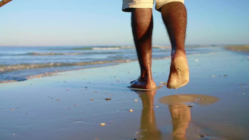 A man walks along the beach as the tide washes over his bare feet