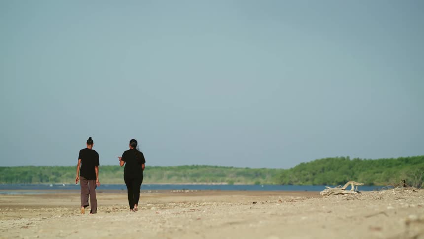 A woman points off in the distance as she and another woman walk and talk on the beach