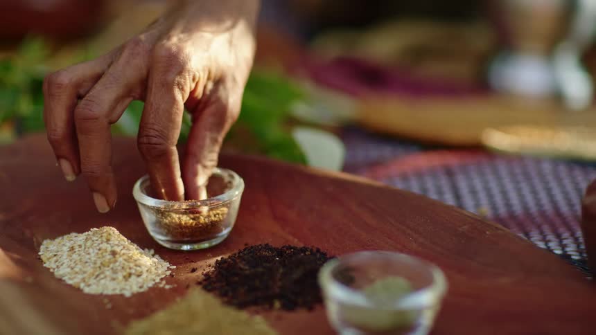 Spices sitting on a board and a woman squeezes some in her fingers