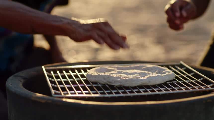 People are cooking damper on a grill