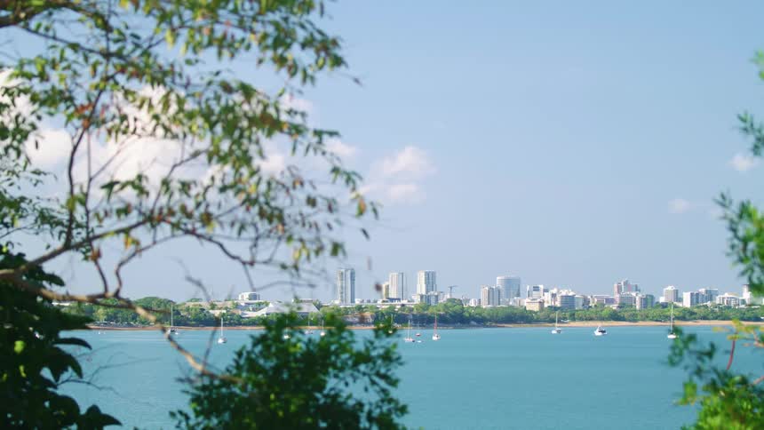 Small boats are floating on a lake on a sunny day with a skyline in the distance