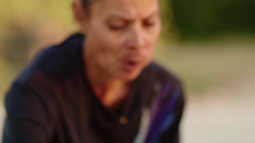 A woman kneels outside in the sand and eats food out of little bowls