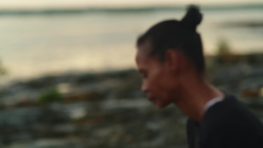 Woman sits on shore looking toward water and the horizon