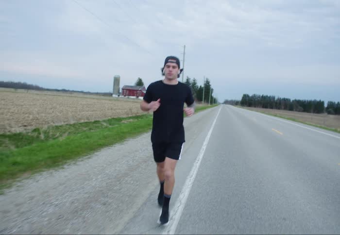Man with a black cap t-shirt and shorts jogs down a country road