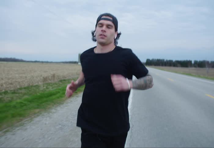 Man with a cap earphones and a black t-shirt jogs on a road in the countryside