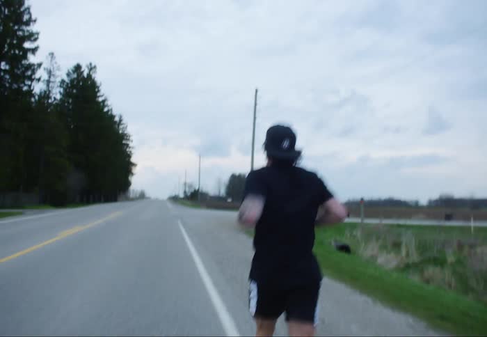 Man with a cap and a t-shirt and shorts jogs on a road in the countryside on a cloudy day